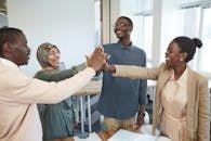 A joyful group of diverse colleagues high-fiving each other in an office, symbolizing teamwork and collaboration.